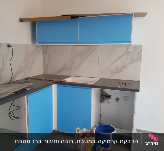 מטבח בשיפוץ עם ארונות כחולים, כיור ודלי צבע